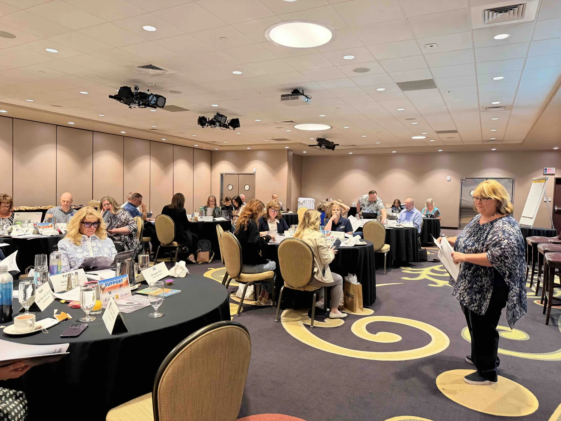 Kelly Rose Hall leading a strategic working session, the room carpet patterned with the Clayton Rose Group swoosh